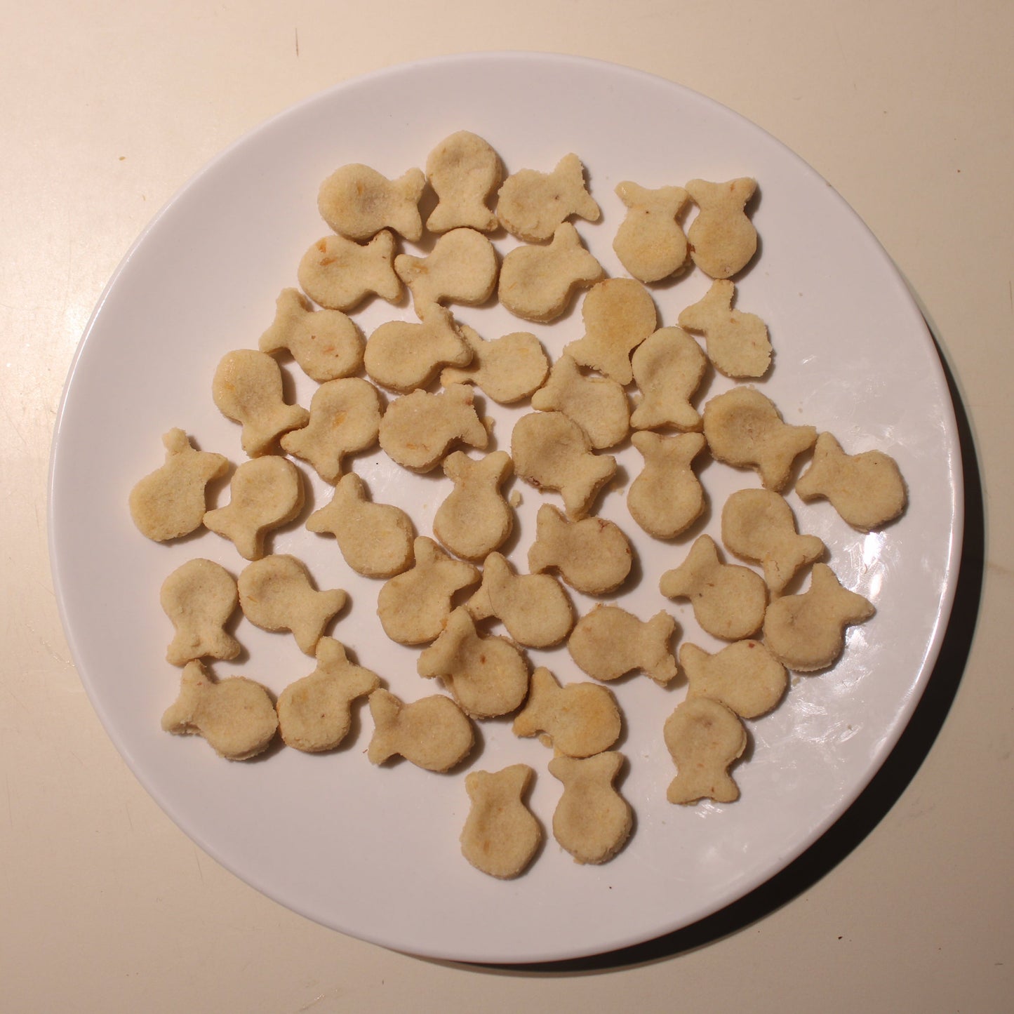 Round white plate with fish-shaped cookies on a beige surface.